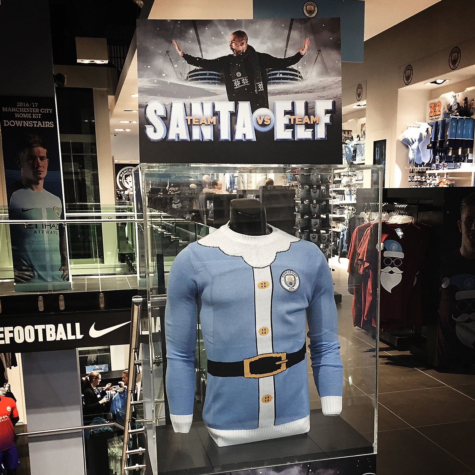 Inside the Manchester City store on Market Street Manchester. A glass cabinet has a Team Santa jumper on display, above a photograph of Pep Guardiola stood with his hands out to the side looking like he is shouting stop