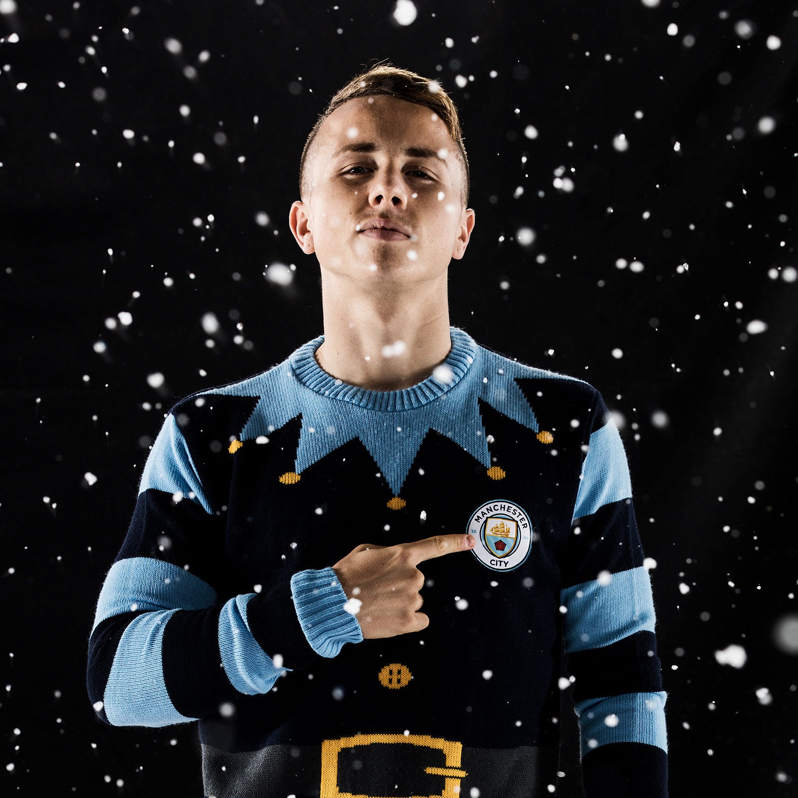 Manchester City player Angelino stood proudly pointing at the City badge on his Elf jumper in a snowy scene