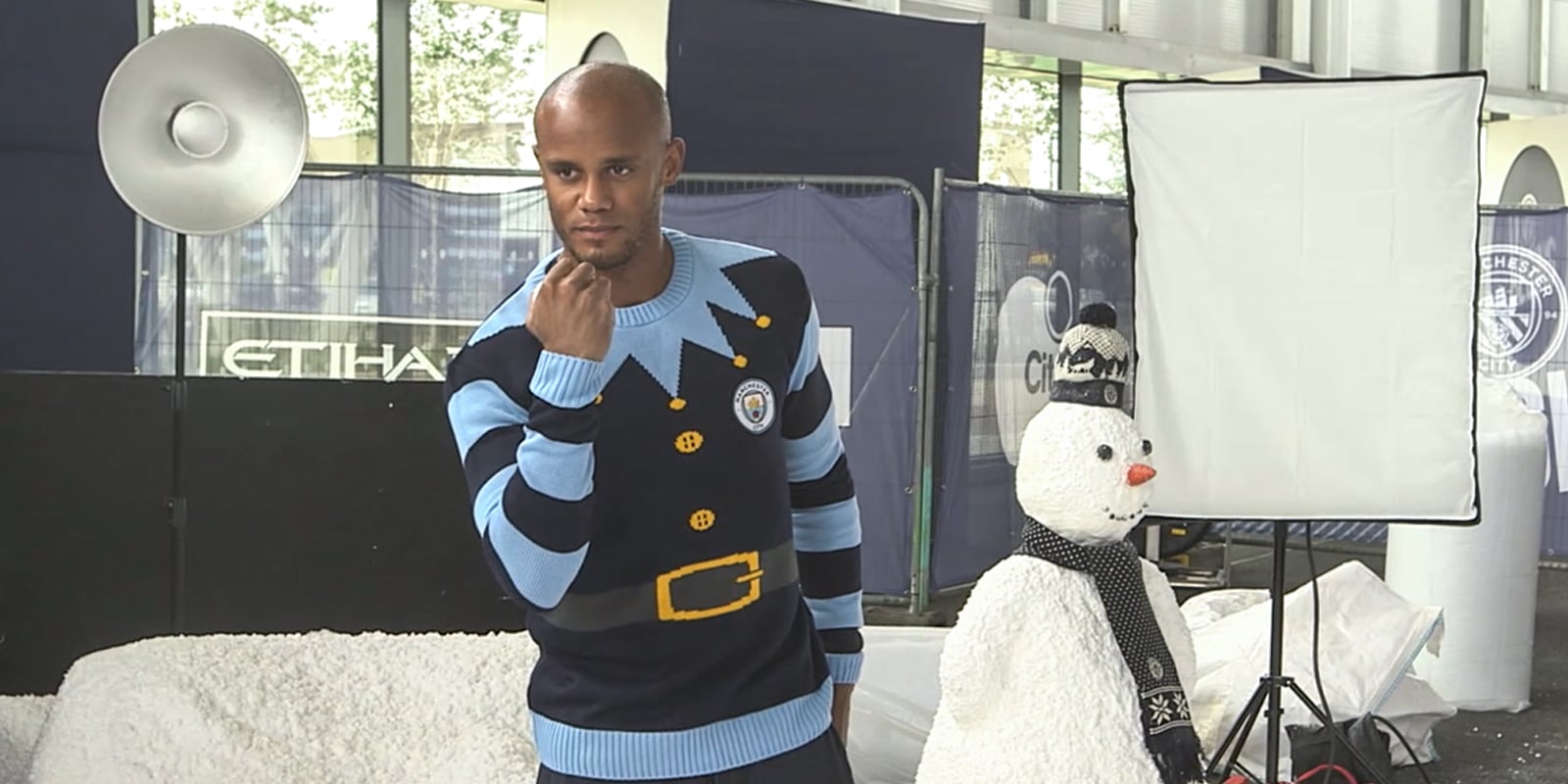 A behind the scenes photograph from the Manchester City Christmas photoshoot, Vincent Kompany stood holding a snowball in front of a snowman