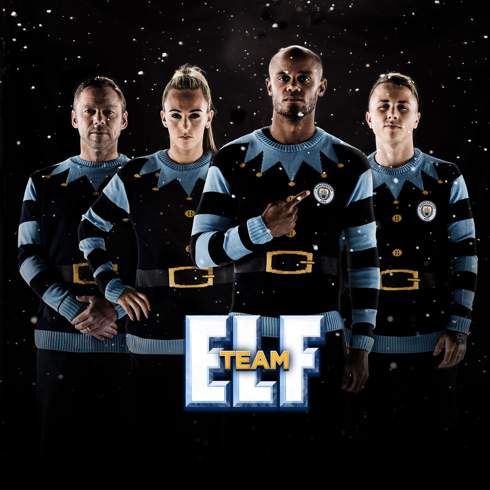 A photograph of Team Elf, Vincent Kompany stood at the front pointing at the Manchester City badge on his jumper. Behind him Toni Duggan, Angelino and Paul Dickov. Snow is falling over a black background behind them