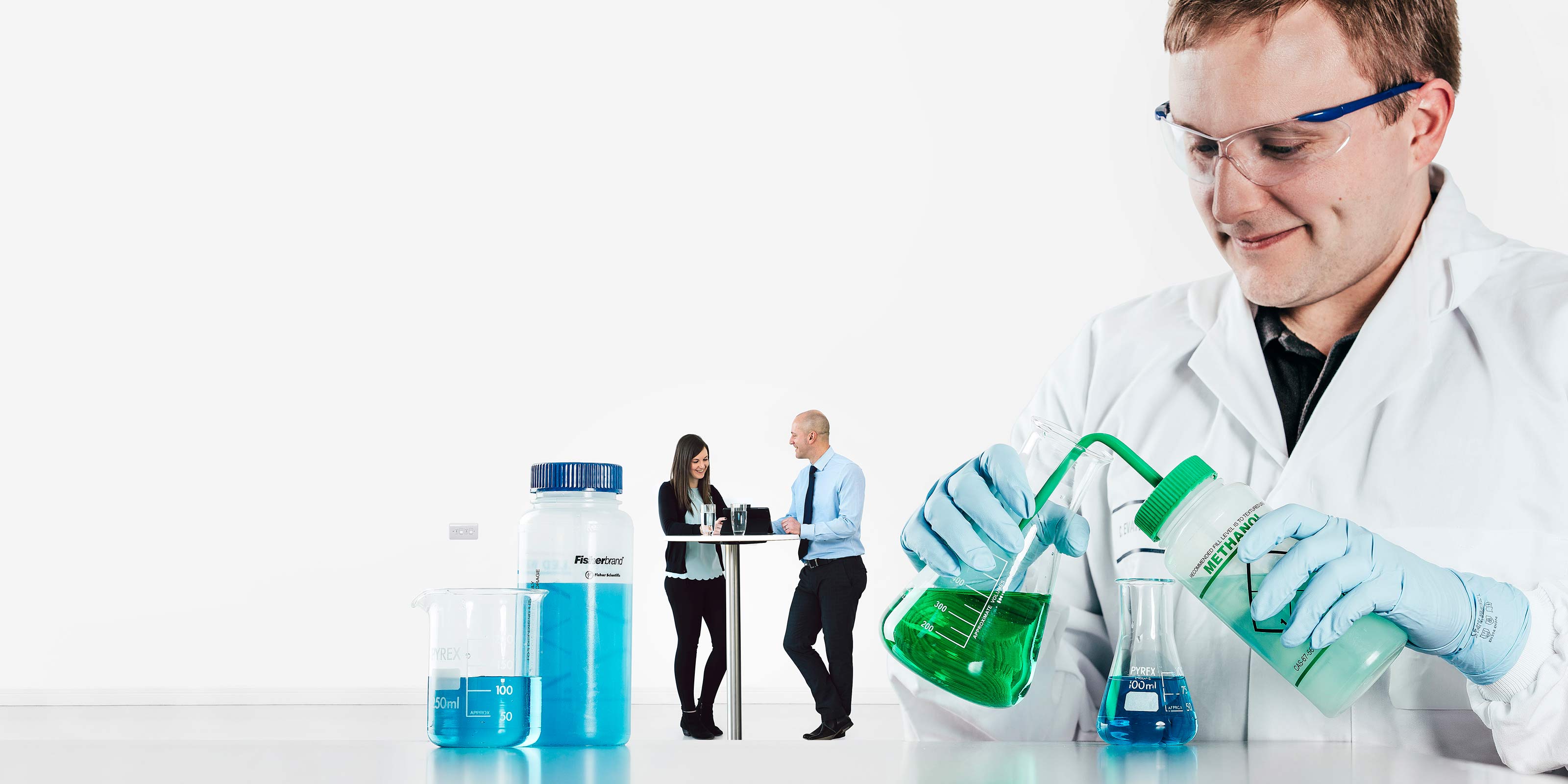 Male scientist working in a lab with people having a meeting in the background